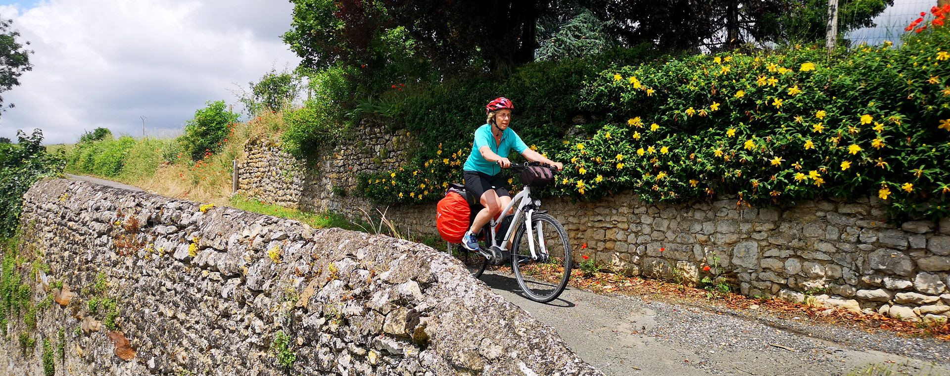 Cycliste sur la Vélo Francette le long d'un muret fleuri - France