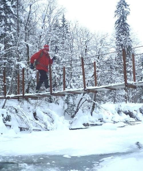 © Raymond Chabanier Randonneur traversant un pont enneigé sur la rivière Subersach - Vorarlberg - Autriche
