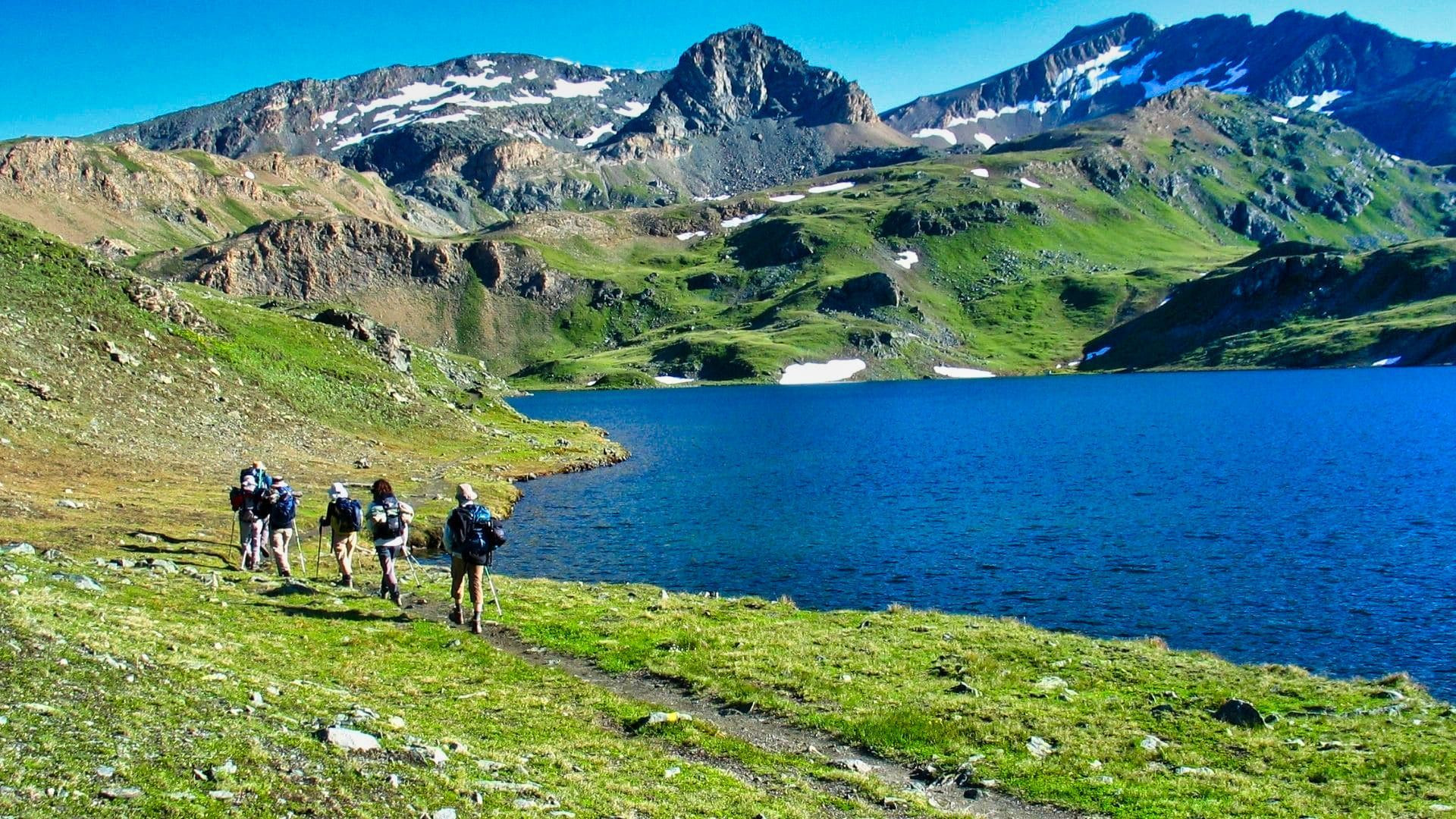 © Jean-Pierre David Randonneurs au bord d'un lac d'altitude sous des sommets enneigés - Grand Paradis - Vallée d'Aoste, Italie