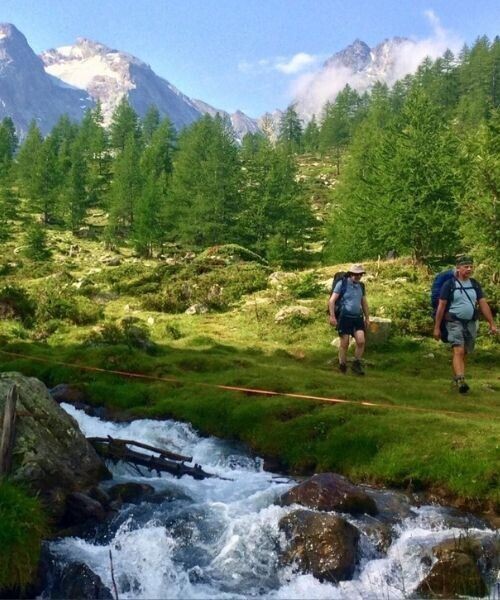 © Laurent Comte Randonneurs traversant un torrent de montagne dans une prairie de mélèzes - Alpes