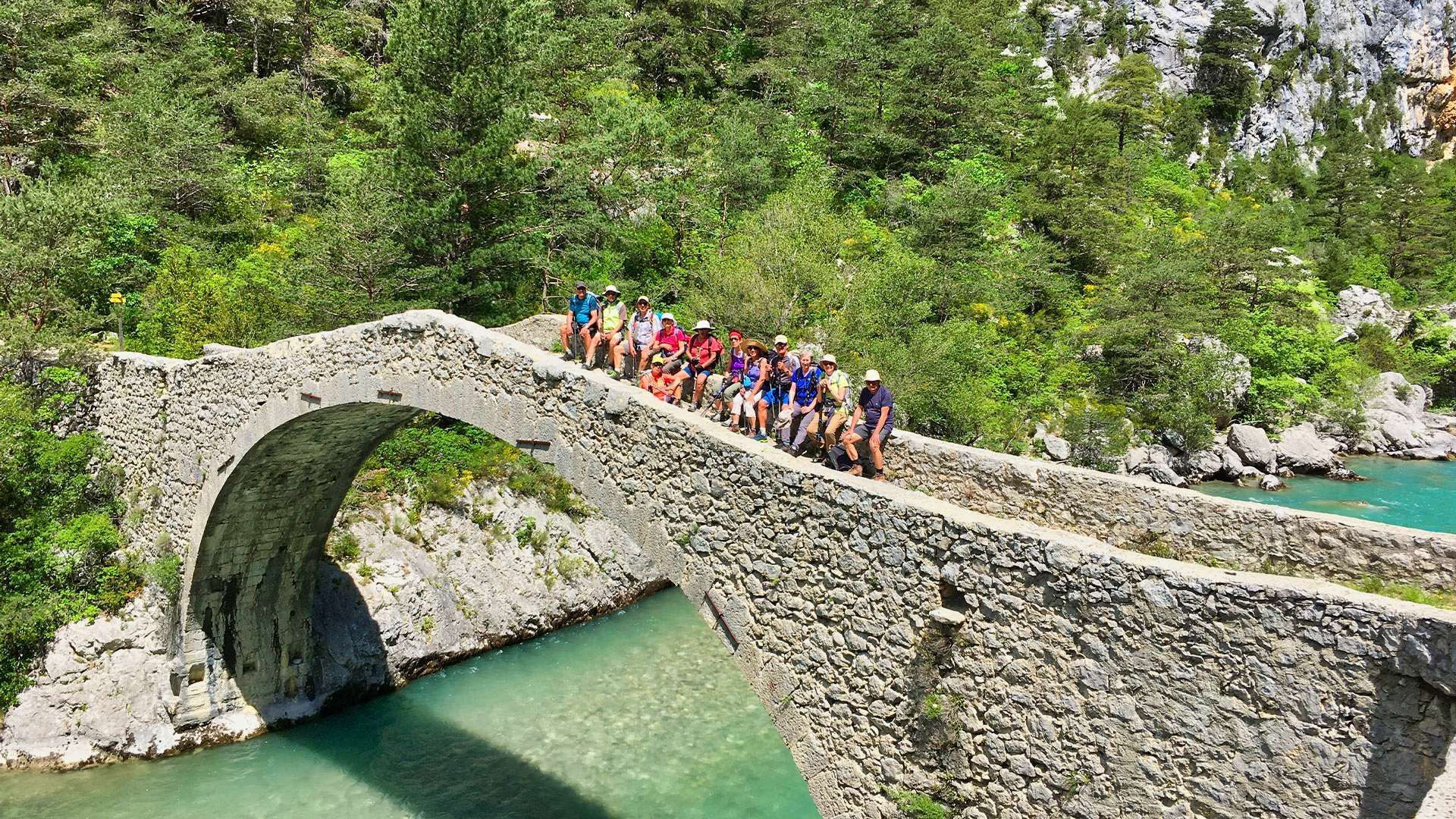 © Jean-Claude Praire Randonneurs sur un pont de pierre au-dessus d'une rivière turquoise