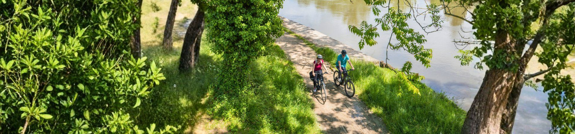 Deux cyclistes sur un chemin ombragé au bord de rivière - France