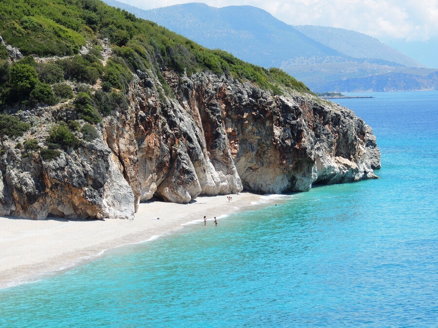Photo de la plage avec du sable blanc et de l'eau turquoise ainsi que des rochers se jetant dans la mer